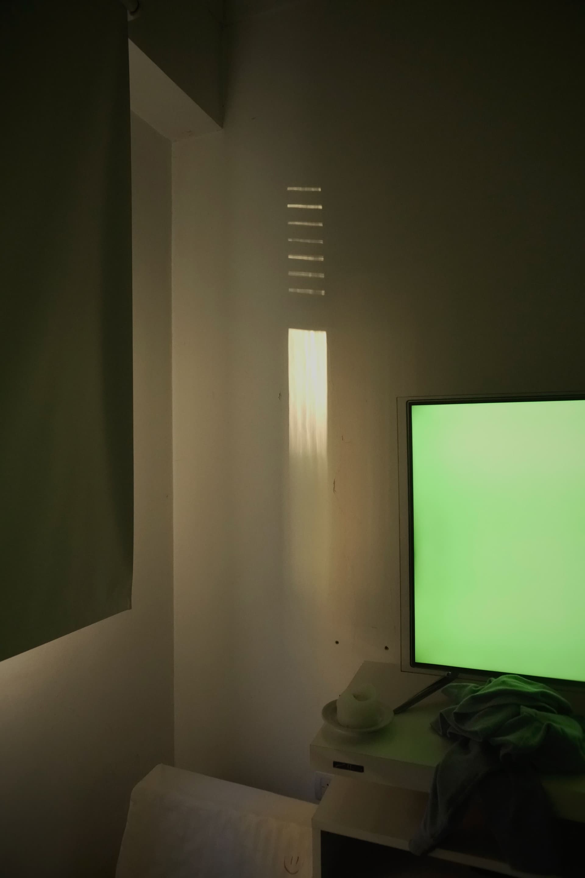 A dimly lit room with a blank television screen throwing soft shadows across the wall.